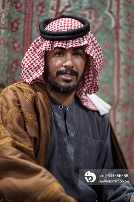 Portrait of Bedouin man wearing traditional headscarf sitting on a carpet in the Saudi desert