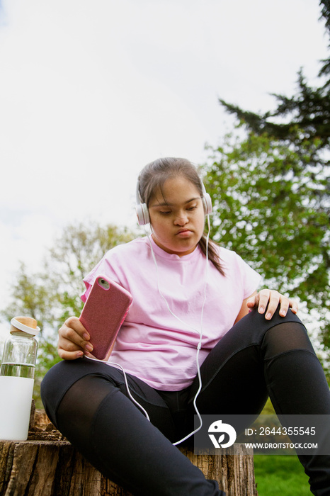 Young curvy girl with Down Syndrome relaxing and listening to music after workout