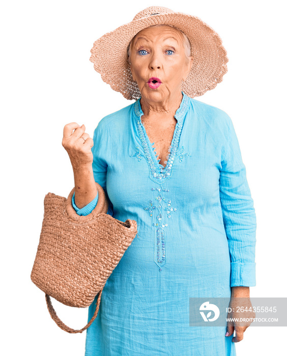 Senior beautiful woman with blue eyes and grey hair wearing fashion dress and hat holding summer wicker handbag scared and amazed with open mouth for surprise, disbelief face