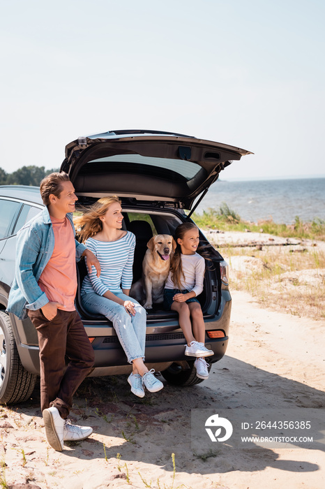 Selective focus of family with golden retriever looking away near auto on beach