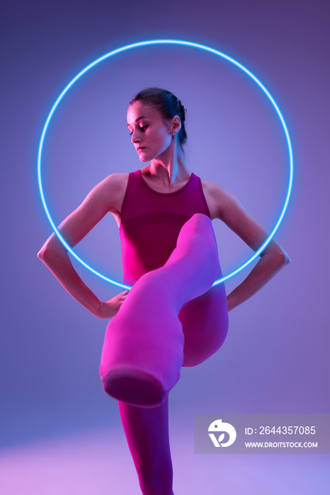 Fashion. Young and graceful ballet dancer isolated on purple studio background in neon light with glowing circle. Art, motion, action, flexibility, inspiration concept. Flexible caucasian ballet