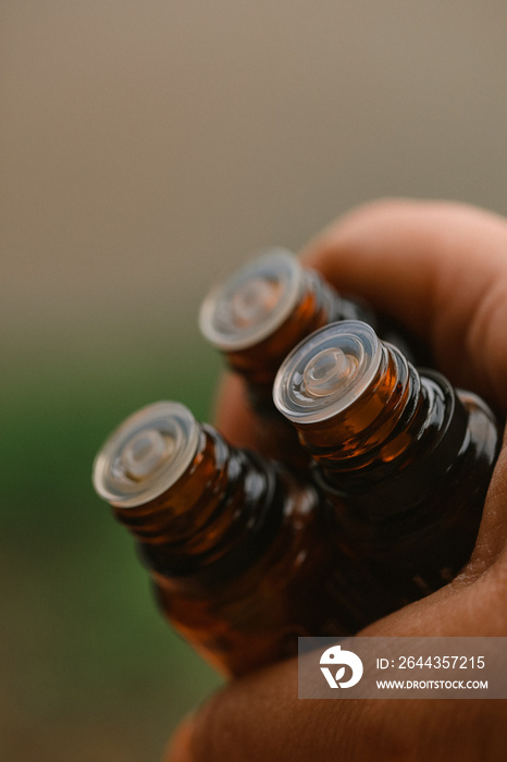 Close up image of hand holding amber essential oil bottles. Bokeh background provides copy space.