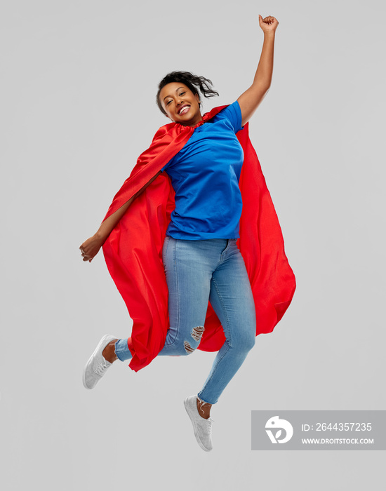 super power and people concept - happy african american young woman in superhero red cape over grey background