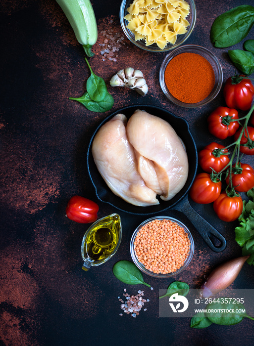 Fresh raw chicken meat, chicken fillet in a pan surrounded by healthy food ingredients on a dark rustic background. Top view, copy space. Vertical