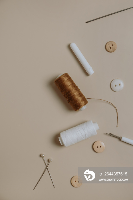 Sewing tools: buttons, spool, threads, needles on neutral beige background.
