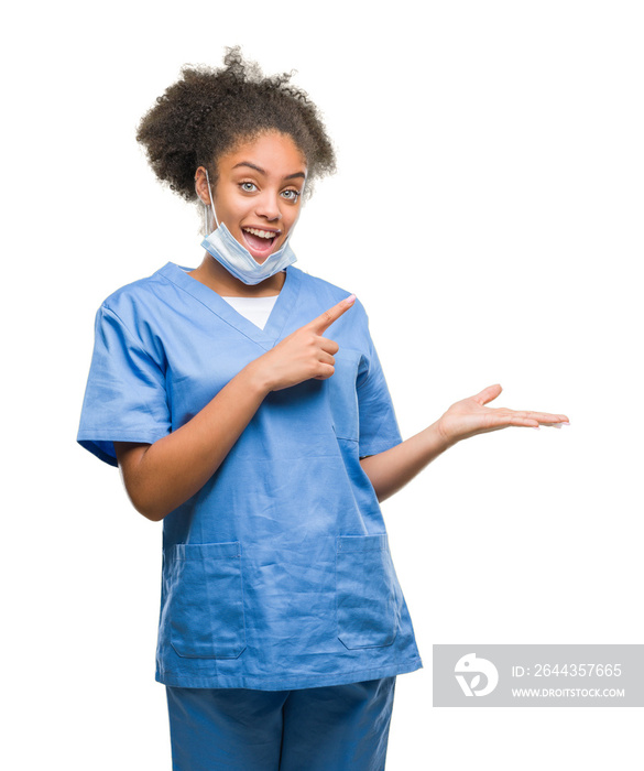 Young afro american doctor woman over isolated background amazed and smiling to the camera while presenting with hand and pointing with finger.