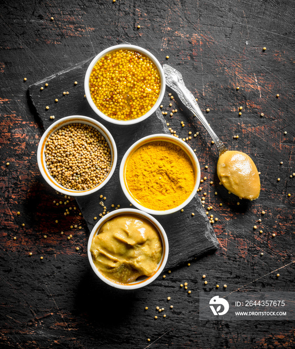 Different types of mustard on a stone Board with a spoon.