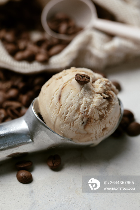 Silver scoop with coffee ice cream and coffee beans on white clay background.