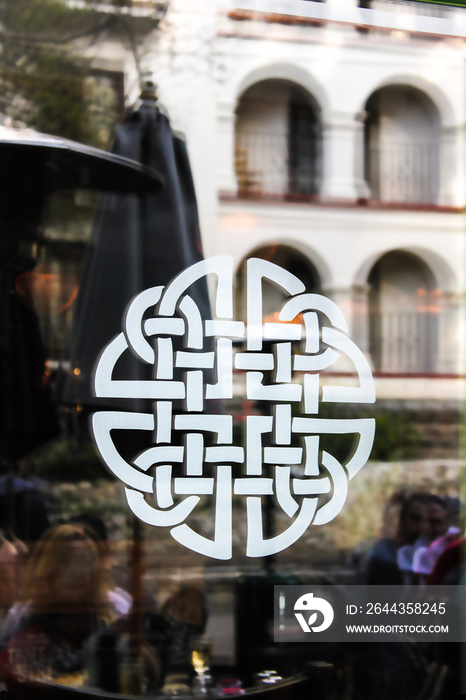 White Celtic Knot on glass door reflecting outdoor restaurant and buildings of San Antonio Tx USA