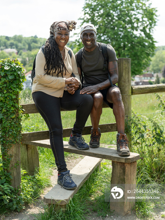 Portrait of smiling mature couple sitting on fence on hike