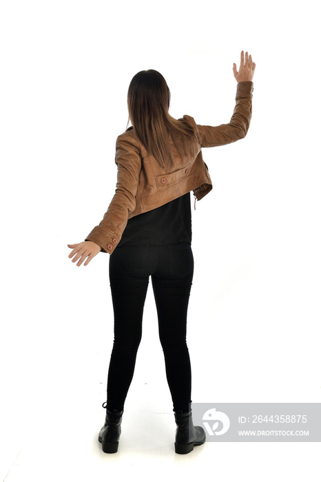 full length portrait of brunette girl wearing brown leather jacket.   standing pose with back to the camera on white background.