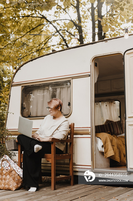 Woman sitting near motorhome RV and working on laptop.