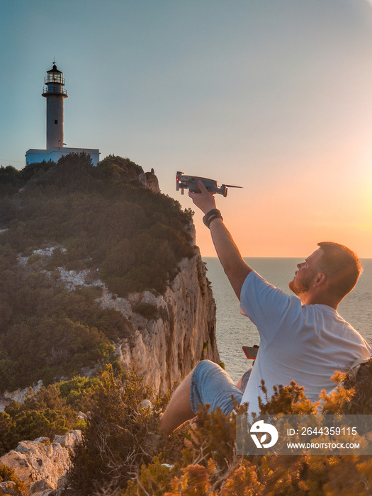 man traveler at the cliff enjoying sunset above the sea light house