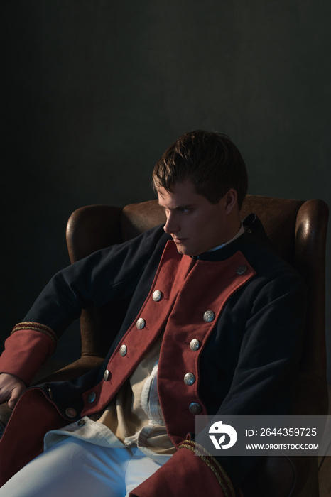 Historical regency man sitting in chair looking aside.