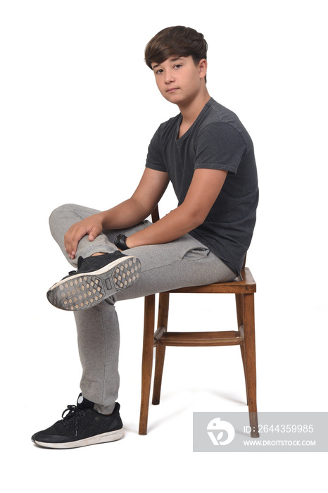 side view of teenage boy sitting on a chair with white background,looking at camera