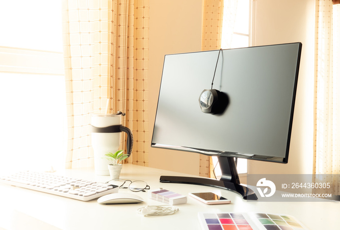 graphic designer work space with Display Calibration, keyboard, color swatch and smartphone on white table with sunlight in the morning.