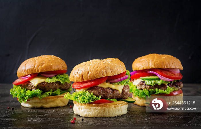 Three hamburger with beef meat burger and fresh vegetables on dark background. Tasty food.