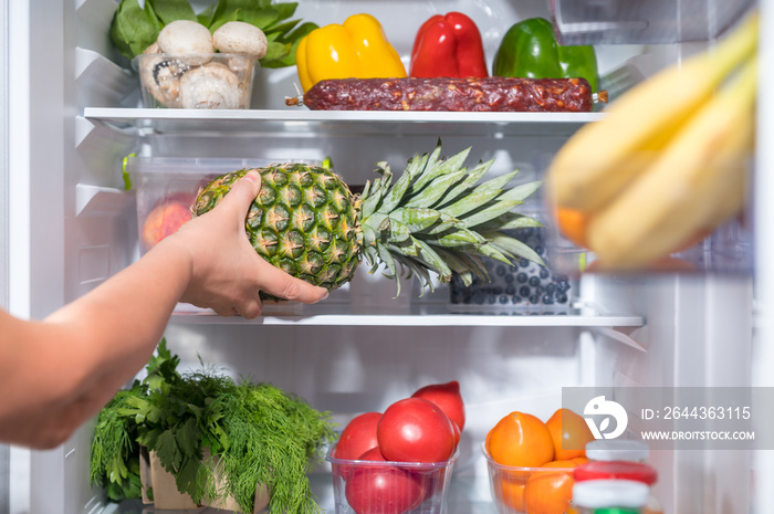 Man putting fresh pineapple into fridge