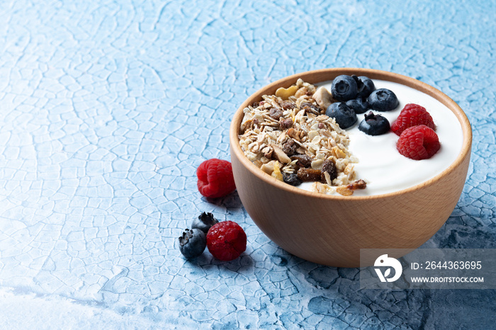 Yogurt with berries and muesli for breakfast in bowl on bue background. Copy space