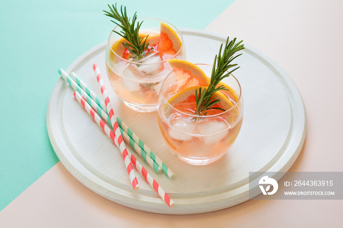 Refreshment grapefruit cocktail with rosemary on white wooden board. Healthy citrus summer drink. Mint and pink colors background