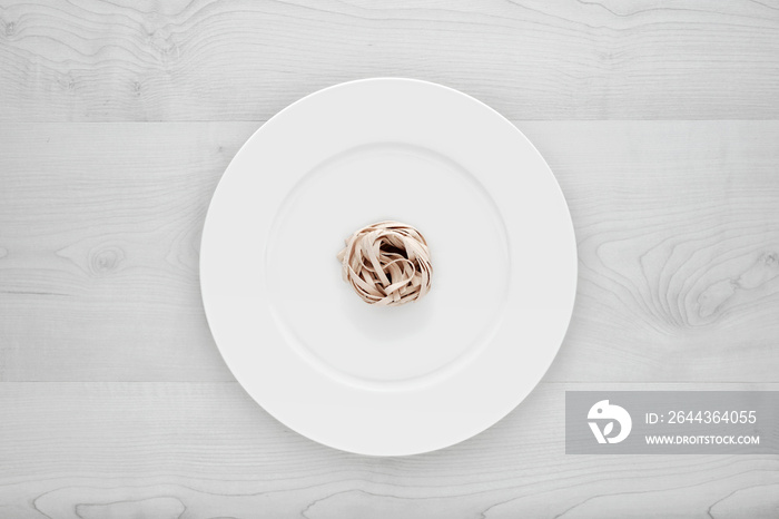 Small portion of tagliatelle pasta on round white plate on a white wooden table. Concept of dieting, healthy and less eating.