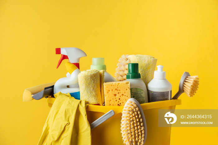 Brushes, bottles with cleaning liquids, sponges, rag and yellow rubber gloves on the yellow background. Cleaning supplies in the yellow bucket. Service of cleaning company advertisement