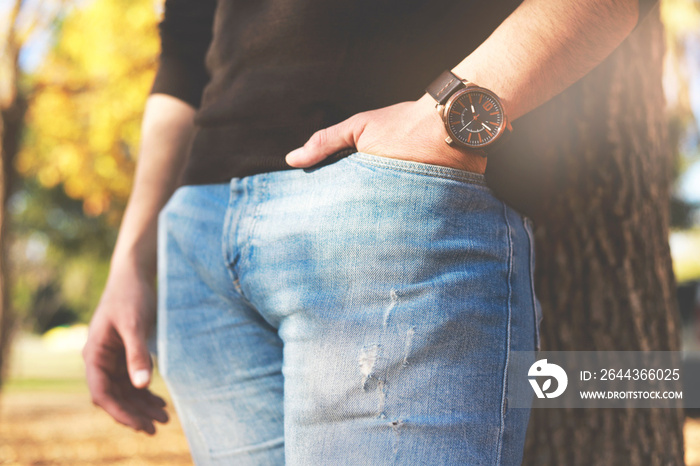 Male hand with a watch in a pocket of trousers. Technology.  Trees on background.