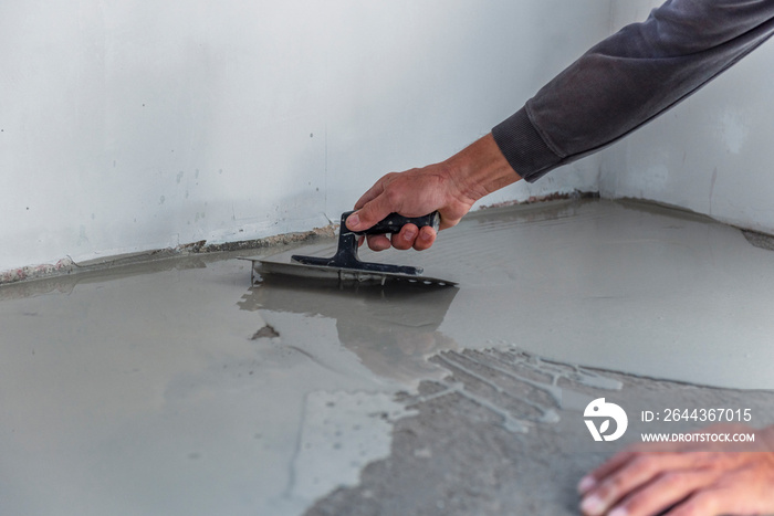 Grey self-leveling screed, new floor layer, man hand.