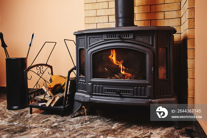 Fireplace and accessories in black with a fire burning inside. Stylish interior, giving warmth in the house.