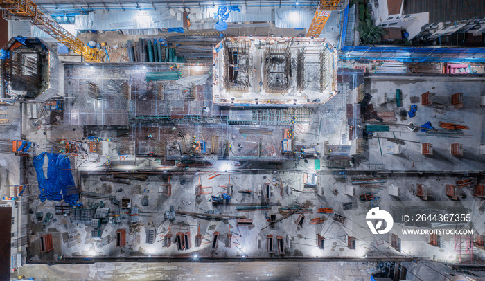 Aerial view of busy industrial construction site workers with cranes working. Top view of development high rise architecture building at night.