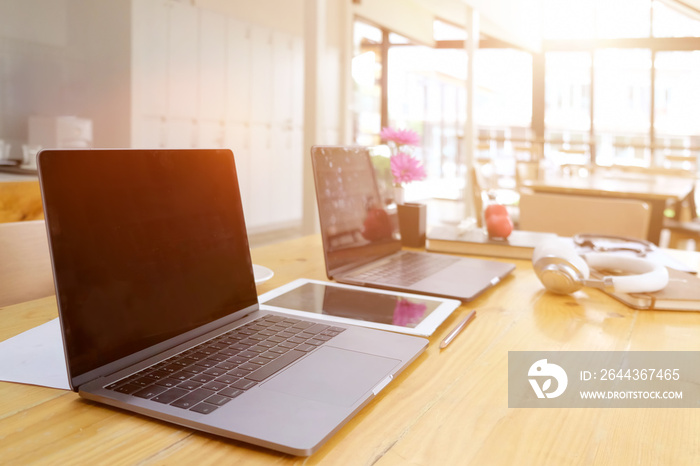 Sideview of office desktop with blank laptop and various office tools on wood desk.