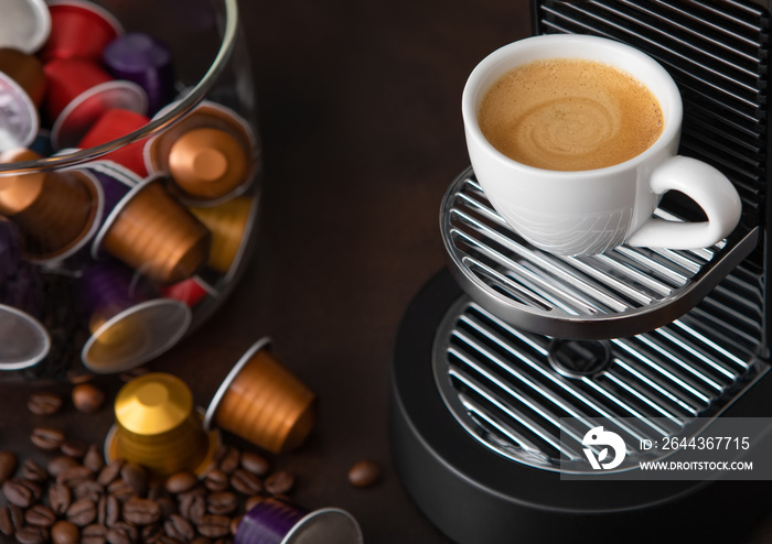 Coffee machine pods capsules with cup and raw aroma coffee beans on brown background.