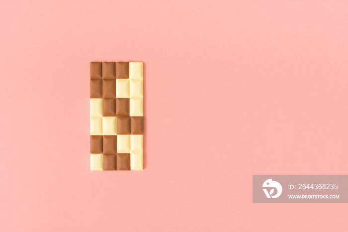 Black and white pieces of chocolate bar on a pastel pink background. Minimal food aesthetic. Creative puzzle concept.