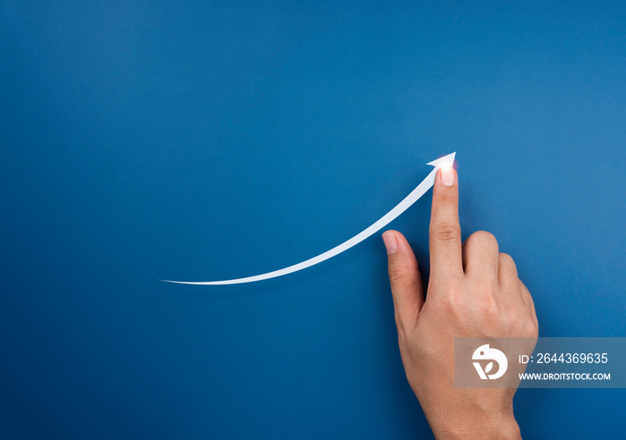 Hand draws a rising arrow on blue background. Finger pointing on the shining arrowhead, minimal style. Business growth and success concept. Increase business opportunities.