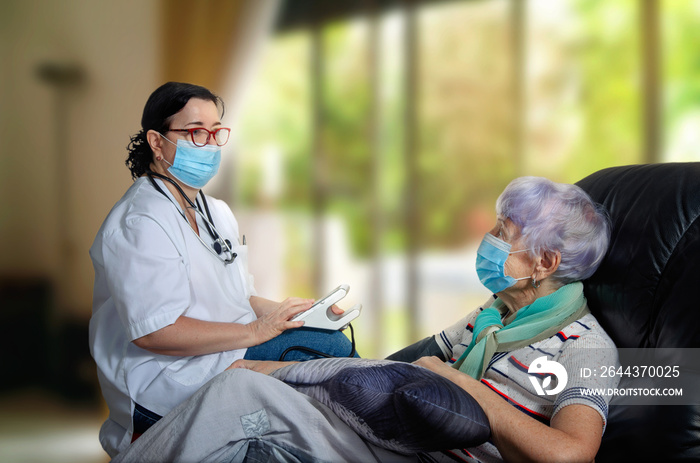 A geriatric doctor visiting an elderly patient at home to take blood pressure. However, both the patient and the geriatrician doctor are required to wear masks during a pandemic.