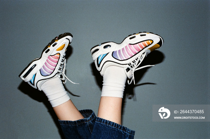 Vintage film photo with grain. Legs in stylish sneakers on a gray wall background, night photo with a flash on a gray background.