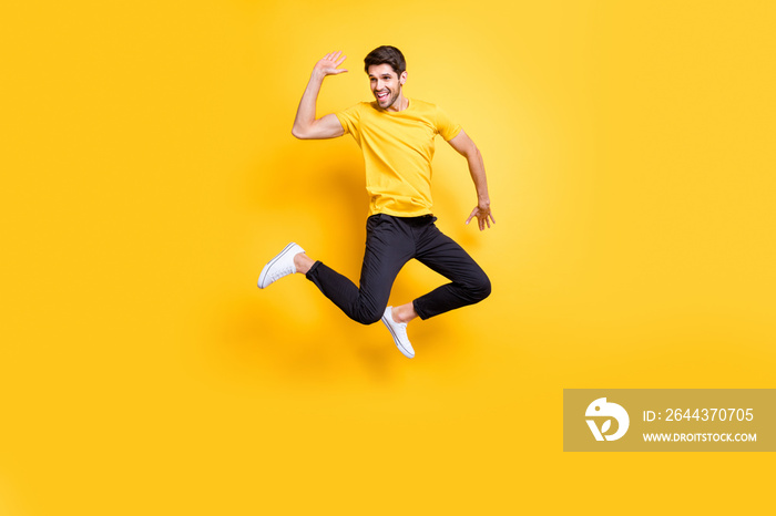 Hi there guys. Full body photo of handsome guy jumping high waving arm see old friends on streets wear casual t-shirt black trousers isolated yellow color background