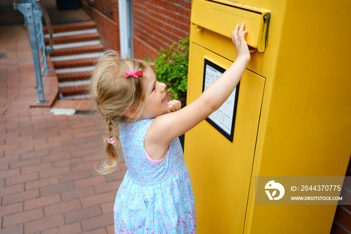 Little preschool girl throwing letter in a mailbox. Excited child writing card or letter for grandparents or family. Old fashioned way of communication.
