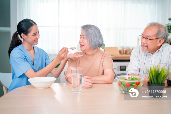 Nurse or doctor who work as homecare staff help to serve a spoon of mush rice to senior woman with her husband sit beside.