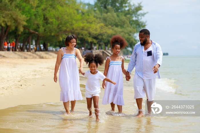 Happy African american family holding hands and walking together on the beach during holiday.