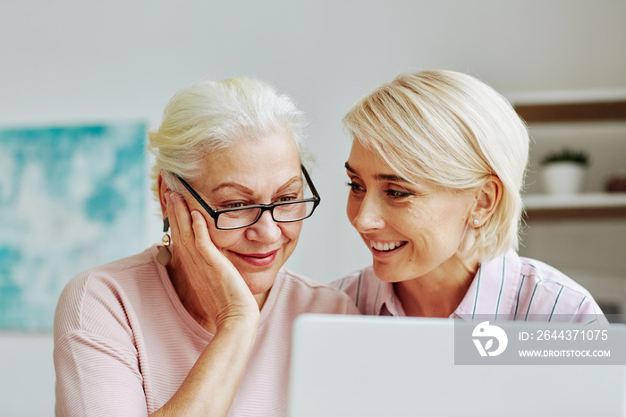 Close up portrait of smiling young woman with senior mother using laptop together at home and shopping online