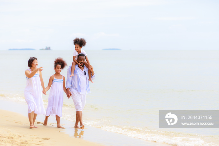 Happy African american family holding hands and walking together on the beach during holiday.