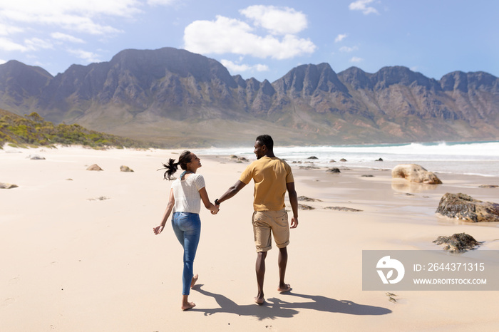 African american couple walking holding hands on a beach by the sea