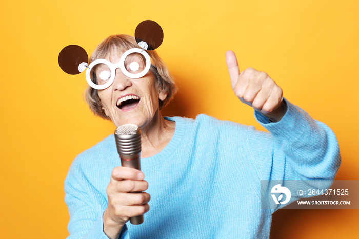 Lifestyle, emotion and old people concept: Happy elderly woman wearing big sunglasses amd holding a microphone and singing