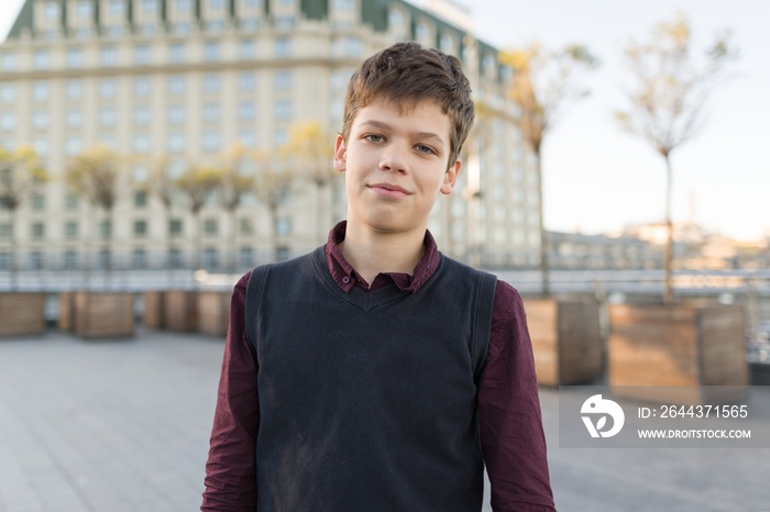 Outdoor portrait of smiling teenager boy 14, 15 years old. City background, golden hour.