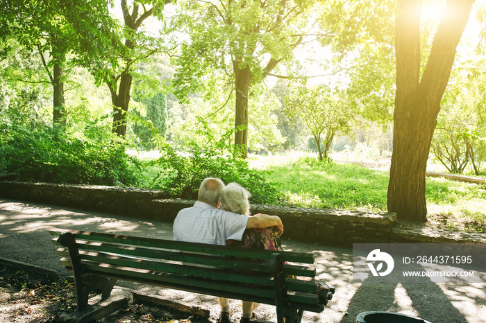 Beautiful old couple is sitting on the bench in the park. Grandma and grandpa are hugging outdoors. Happy golden wedding anniversary. Romantic photo of grandmother and grandfather. Real love.