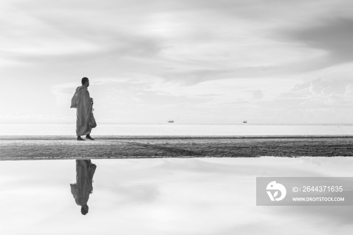 Monk receiving food and walking on the beach in the morning in Thailand