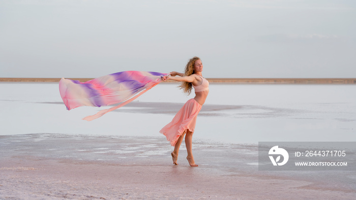 beautiful graceful girl in the rays of pink sunset light on the seashore keeps a pareo developing in the wind. lightness, freedom