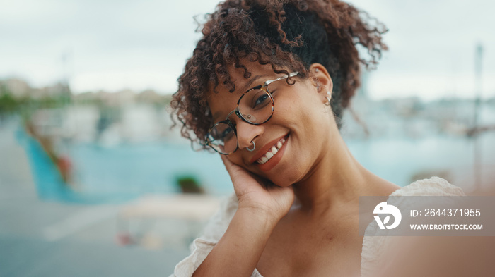 Closeup of a young woman in glasses stands in the seaport and shots selfie on smartphone. Positive woman using mobile phone outdoors in urban background.