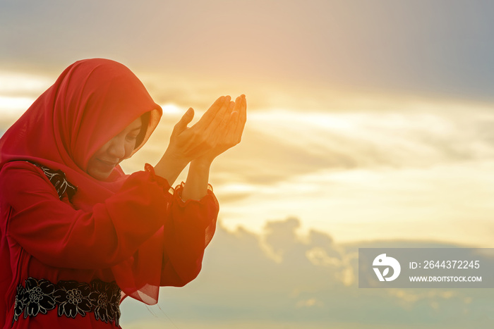 Veiled Islamic muslim woman wearing a burka standing and praying in the sunset